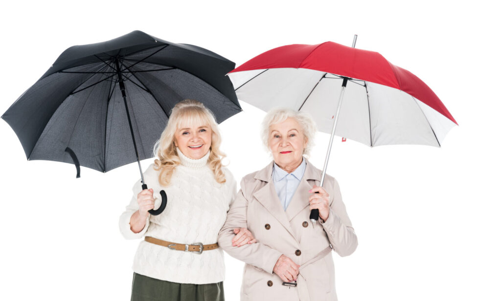 cheerful Medicare Aged women standing under umbrellas